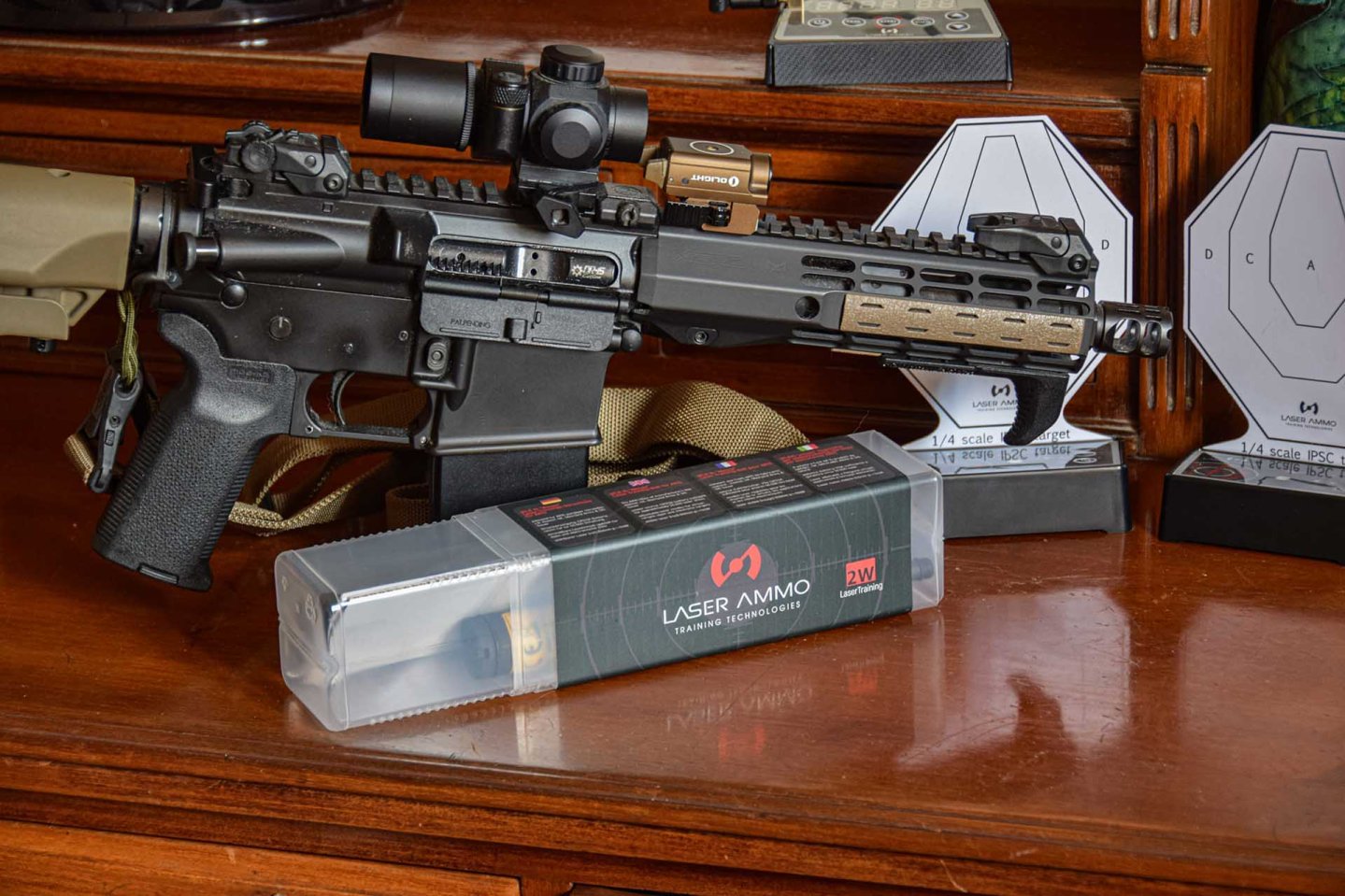 Laser Ammo: Neue Produkte für den Herbst 2022 – CQB in a Box, Shot on Body und Flash Bolt BCG Flash Bolt BCG Laser Verschlussträger mit AR-15 im Hintergrund.
