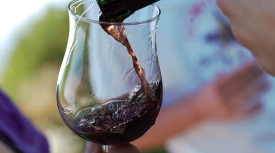 Rotwein wird bei Wanderung durch Weinberg in ein Rotweinglas gefüllt