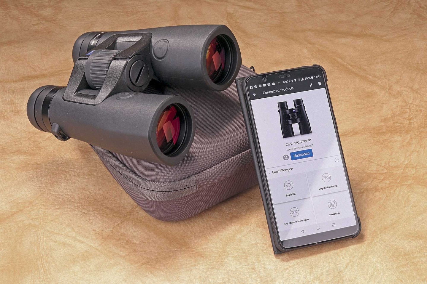 Das ZEISS Victory RF 10x42 Fernglas liegt auf seiner Tasche neben Smartphone, auf dem die ZEISS Hunting App aktiv ist.