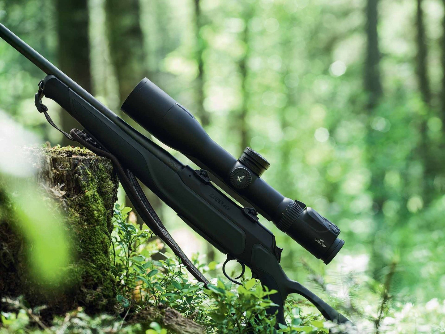 Das Zielfernrohr Swarovski Optik dS gibt's nun auch mit SR Schienenmontage Gewehr mit Swarovski Optik dS 5-25x52 P an einen Baum gelehnt