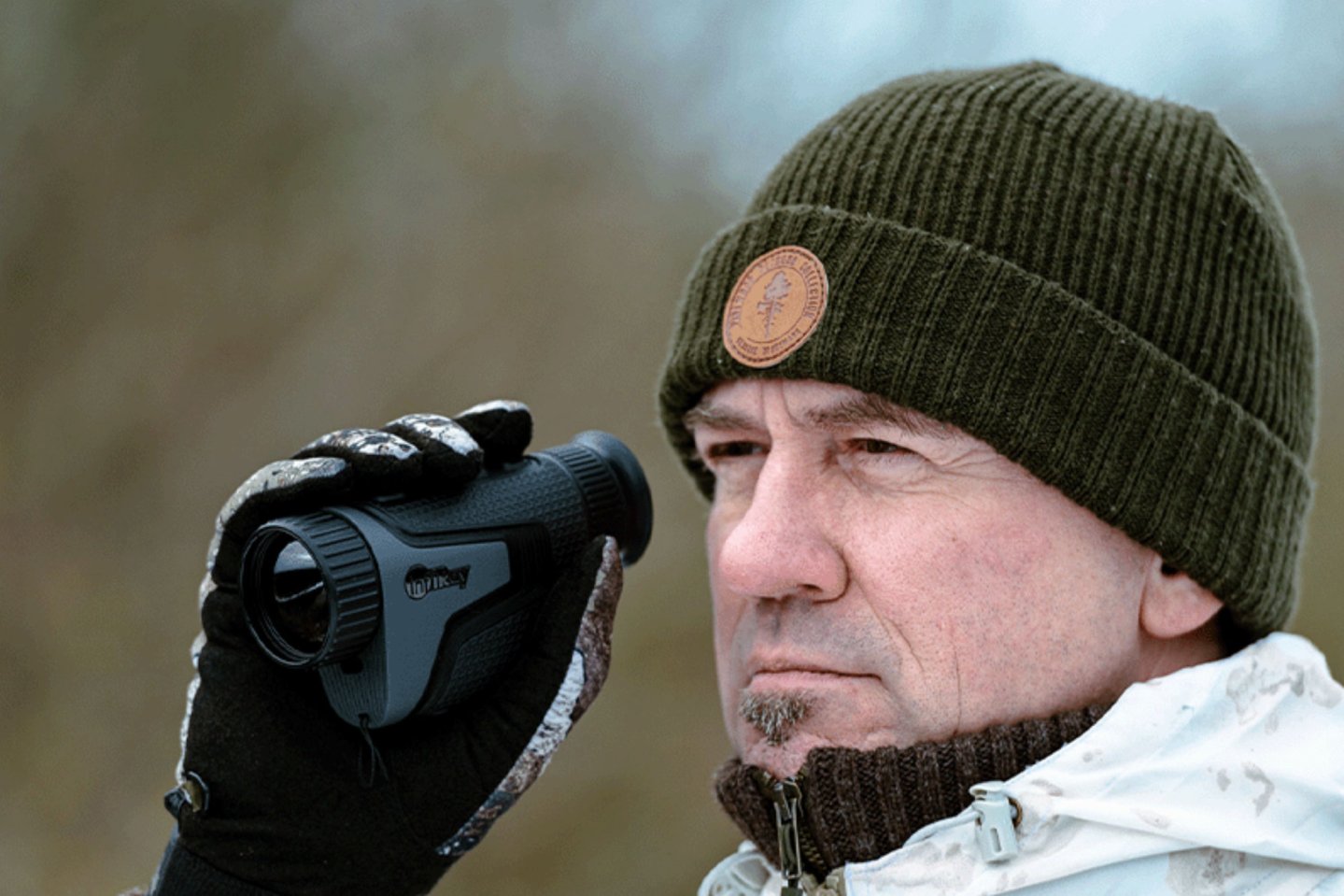 Ein Jäger im Schneetarnanzug sucht mit dem InfiRay Iris IL35 das Gelände ab.
