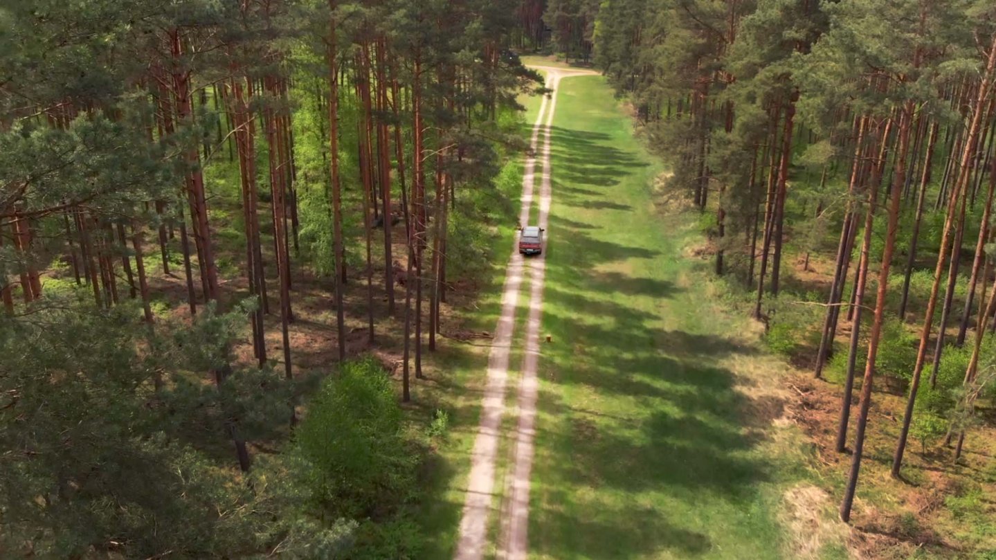 Eine Vogelperspektive eines Waldstückes und einem Fahrzeug welches dort entlangfährt.