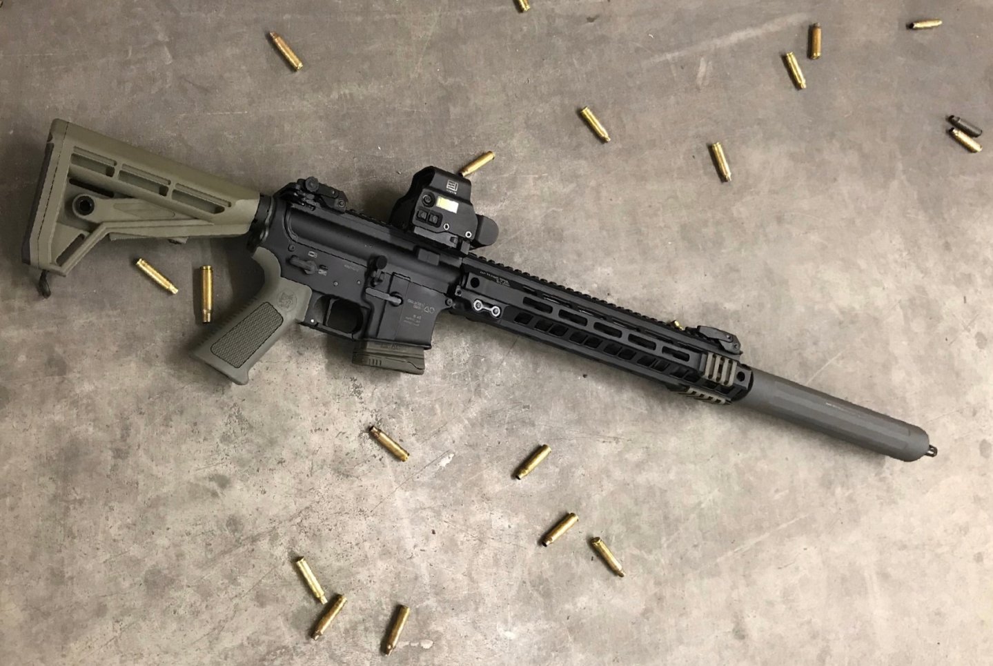 Im Praxistest von Hanna Selena: Oberland Arms KDA Schalldämpfer für die Jagd mit Halbautomaten OA-15 Selbstladebuechse von Oberland Arms liegt mit montiertem KDA Schalldaempfer auf Beton und ist von Huelsen umgeben