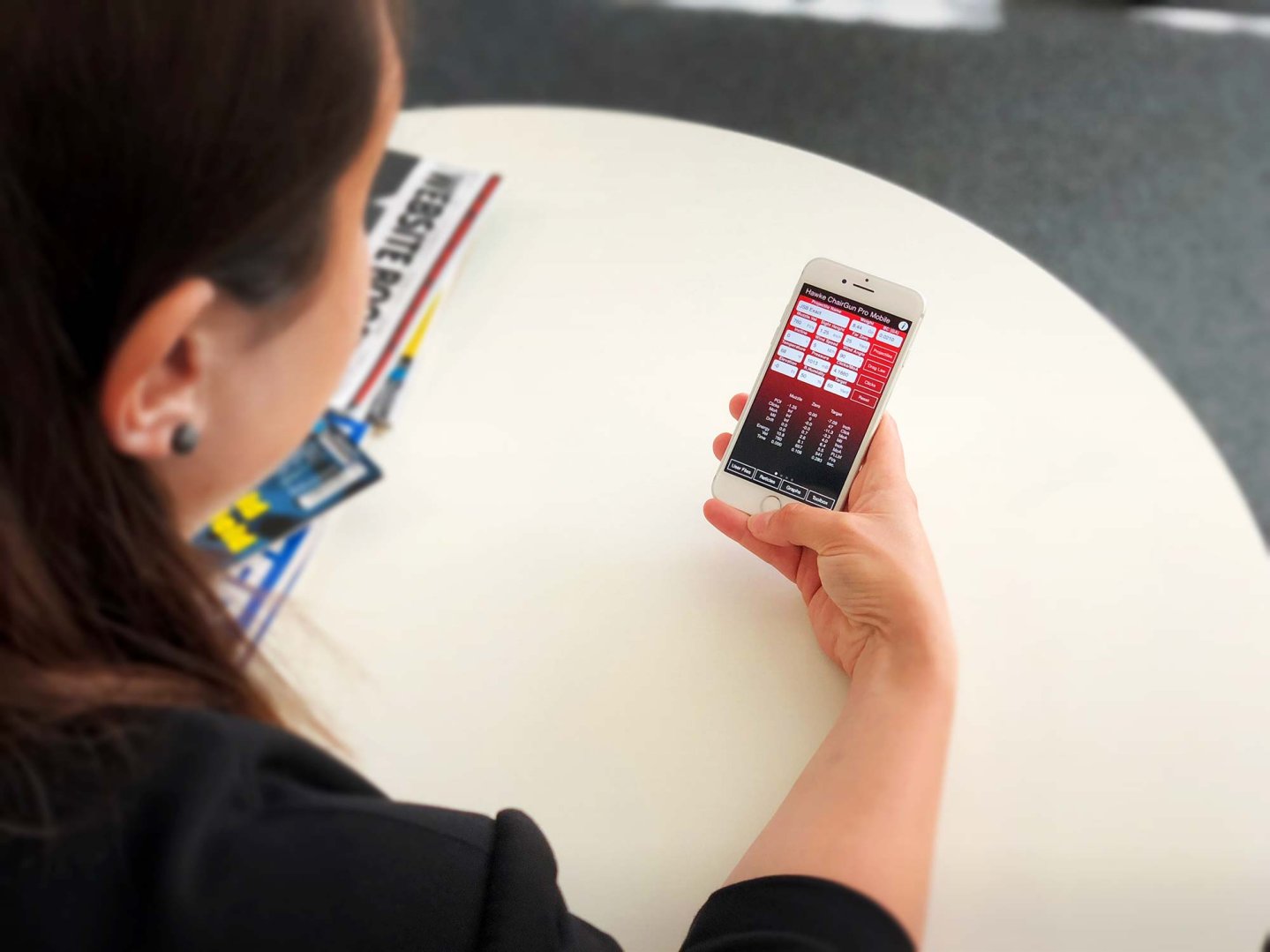 Hawke Chairgun Pro Mobile User Eine Nutzerin sitzt an einem Tisch und hat die Hawke Chairgun Pro Mobile App auf ihrem iPhone geöffnet.