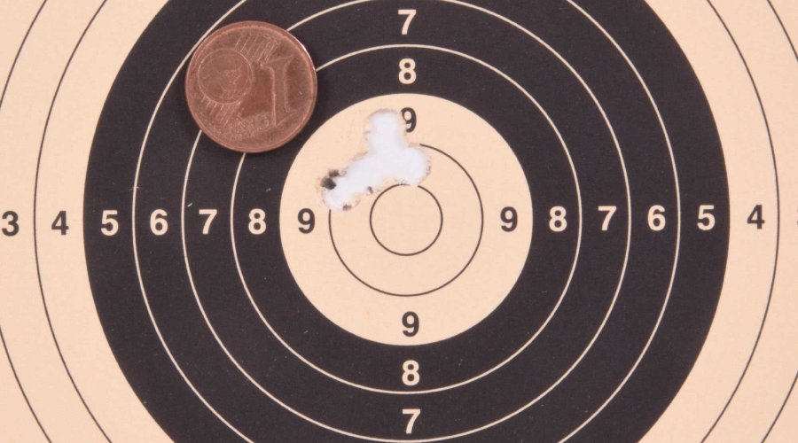 Beschossene Zielscheibe mit Trefferbild von 10 mm auf 100 m Entfernung und 1 Cent-Münze als Referenz für die Größe des Streukreises