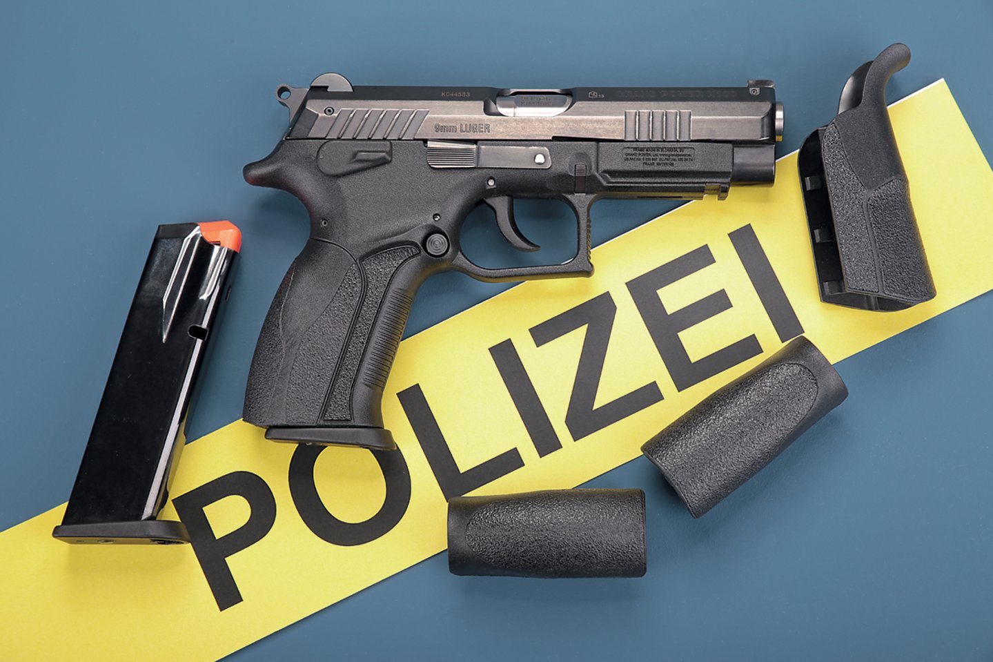 Test: Grand Power K 100 in 9 mm Luger Grand Power K 100 liegend auf Tisch mit Polizei-Schild