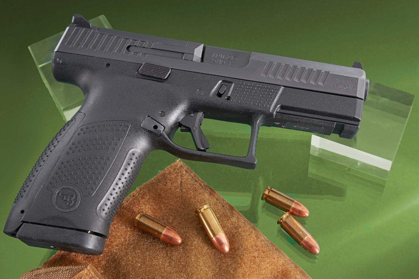 Test: Polymerpistole CZ P10 C OR CZ P10 C OR von rechts auf grünem Untergrund. Davor vier Patronen in 9 x 19 mm auf einem Stück Leder.