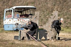 3. International Bodyguard Conference 2018 Zwei Teilnehmer mit AR-15-Gewehren bringen sich vor Spanplatten in Stellung, dahinter ein zerschossener Bus.