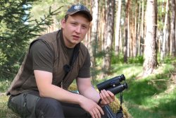 GECO Gold 10x42 und 10x50: die Ferngläser in der Jagdpraxis Jäger sitzt mit im Wald und hält ein GECO Gold Fernglas in der Hand
