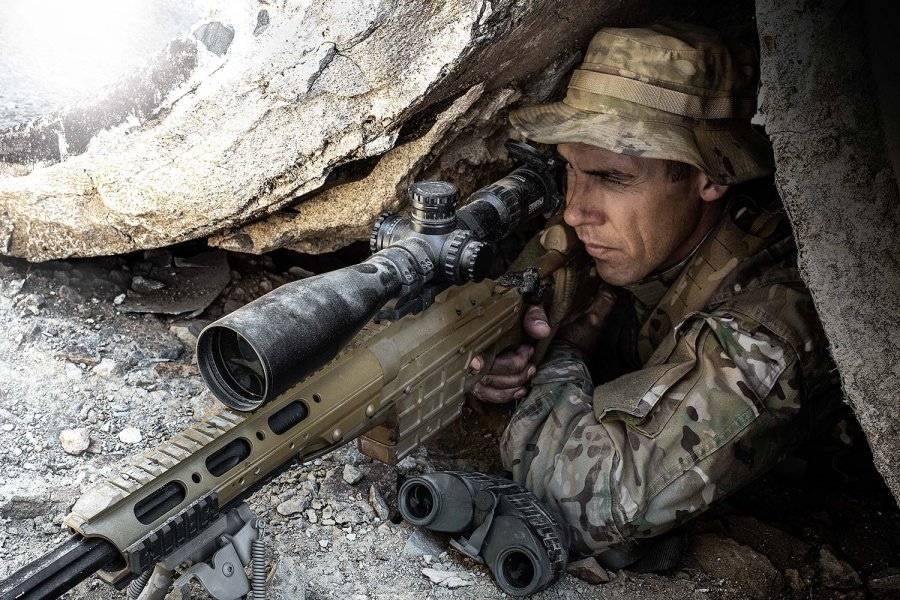 Scharfschütze mit Steiner M5Xi 5-25x56 im Einsatz Ein Scharfschütze zielt zwischen einer Felsspalte hervor, dabei ist sein Gewehr mit dem montierten Steiner M5Xi 5-25x56 Zielfernrohr deutlich erkennbar.