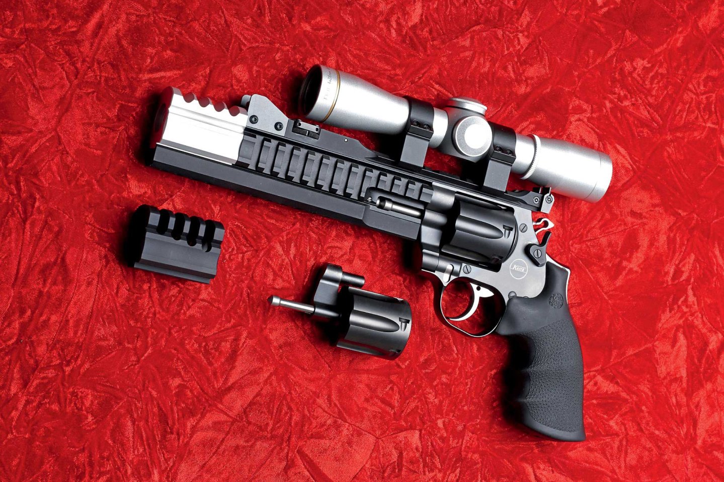 caliber 2/2017 Korth Super Sport 1400 in linker Seitanansicht auf rotem Grund mit Wechseltrommel, Kompensator und Zielfernrohr.