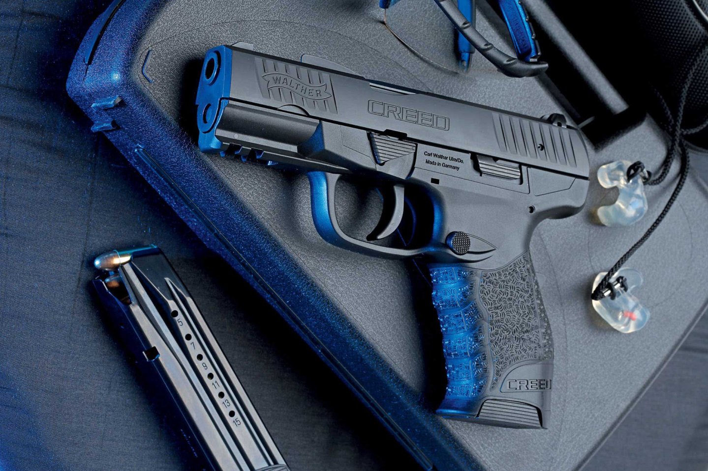 caliber 5/2017 Walther Creed in linker Seitenansicht auf einem schwarzem Pistolenkoffer mit Gehörschutz und Magazin.