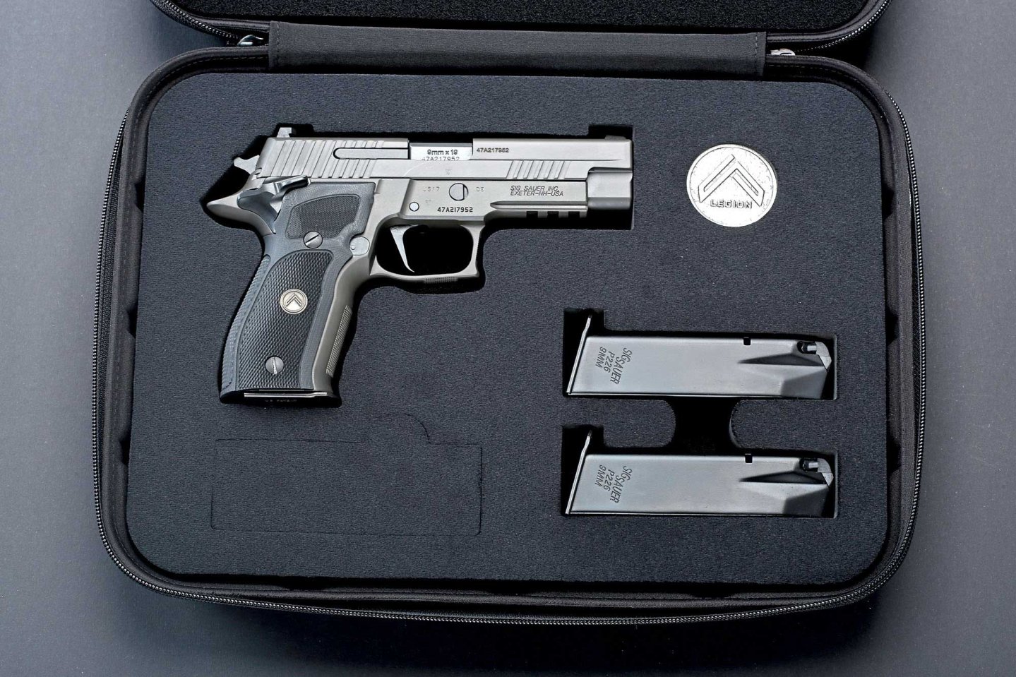 caliber 6/2017 SIG Sauer P226 Legion SAO in rechter Seitenansicht im Pistolenkoffer mit zwei Ersatzmagazinen und eine Medaille.