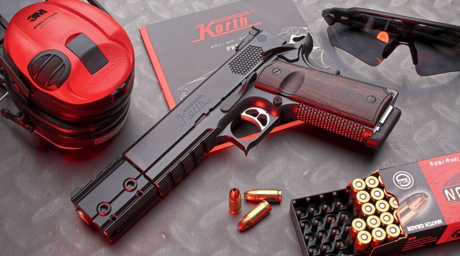 caliber 9/2016 Korth PRS mit Gehörschutz, Bedienungsanleitung, Schießbrille und 9mm-Luger-Munition auf grauer Platte.