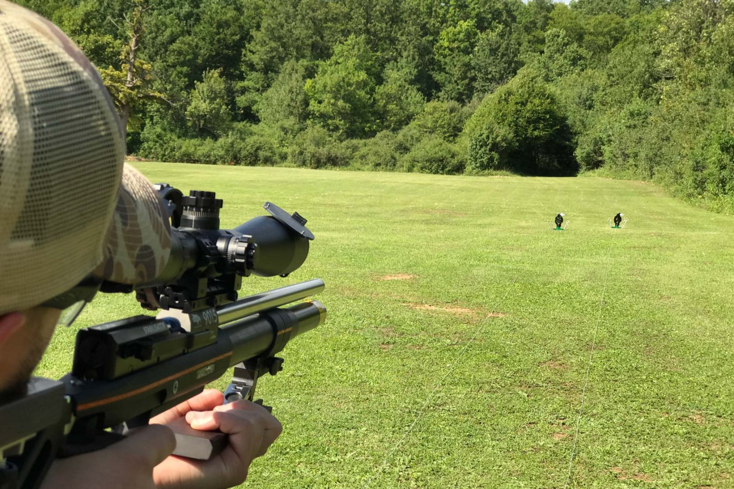 Field-Target-Schütze visiert mit Luftgewehr mit Zielfernrohr Stahlziele in der Entfernung an