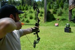 Ausrüstung fürs Bogenschießen – Bogensport mit 4komma5 Bogenschütze zielt mit Compoundbogen auf 2 Ziele in Würfelform und einen roten Range Bag Zielsack im Freien