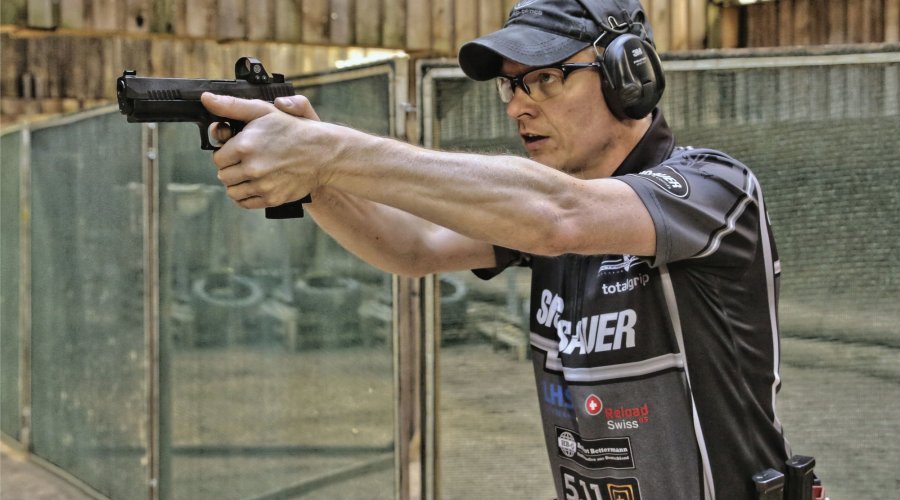 Schütze im Anschlag beim dynamischen Sportschießen. Auf der Pistole befindet sich ein Leuchtpunktzielgerät.