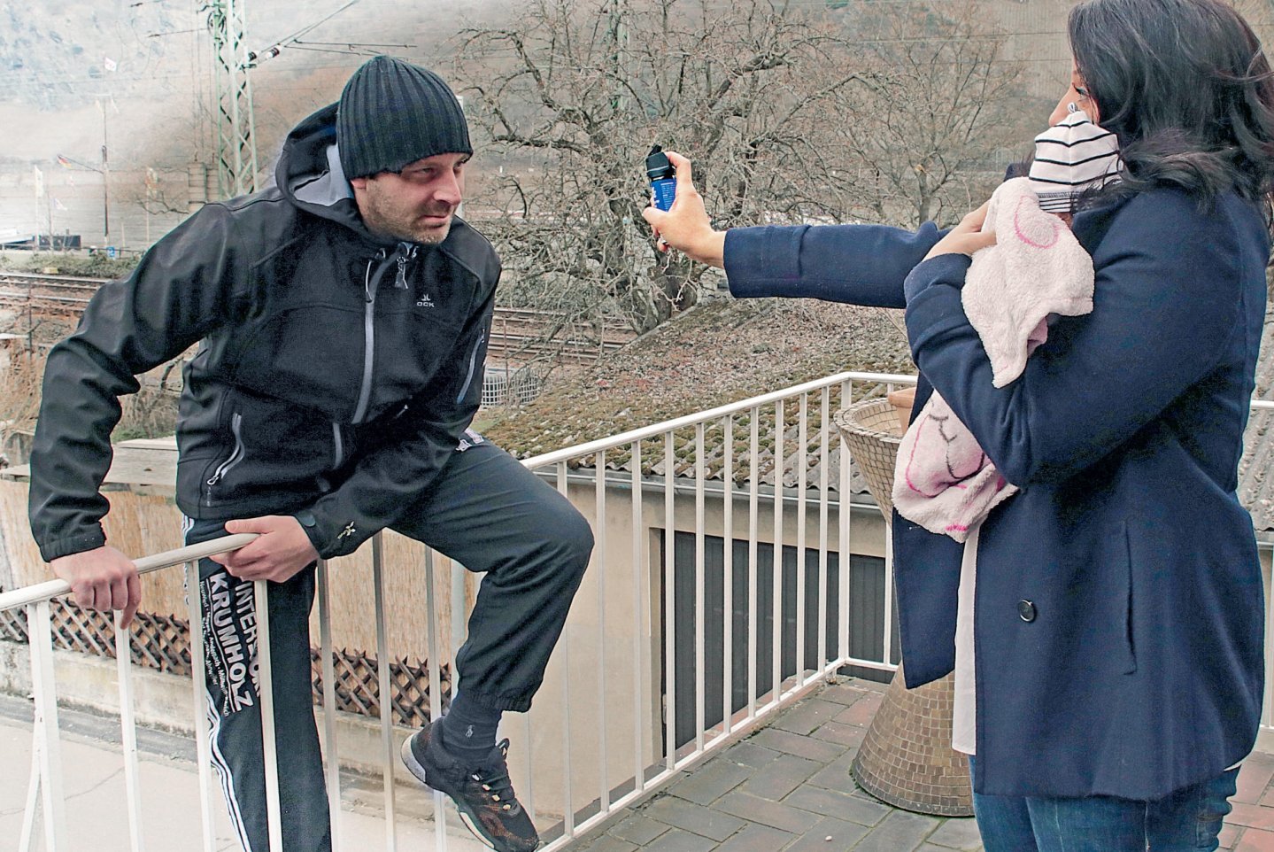 Ein Mann übersteigt ein Geländer um eine Frau mit Kind auf dem Arm anzugreifen. Die Frau setzt sich mit einem Pfefferspray zur wehr.
