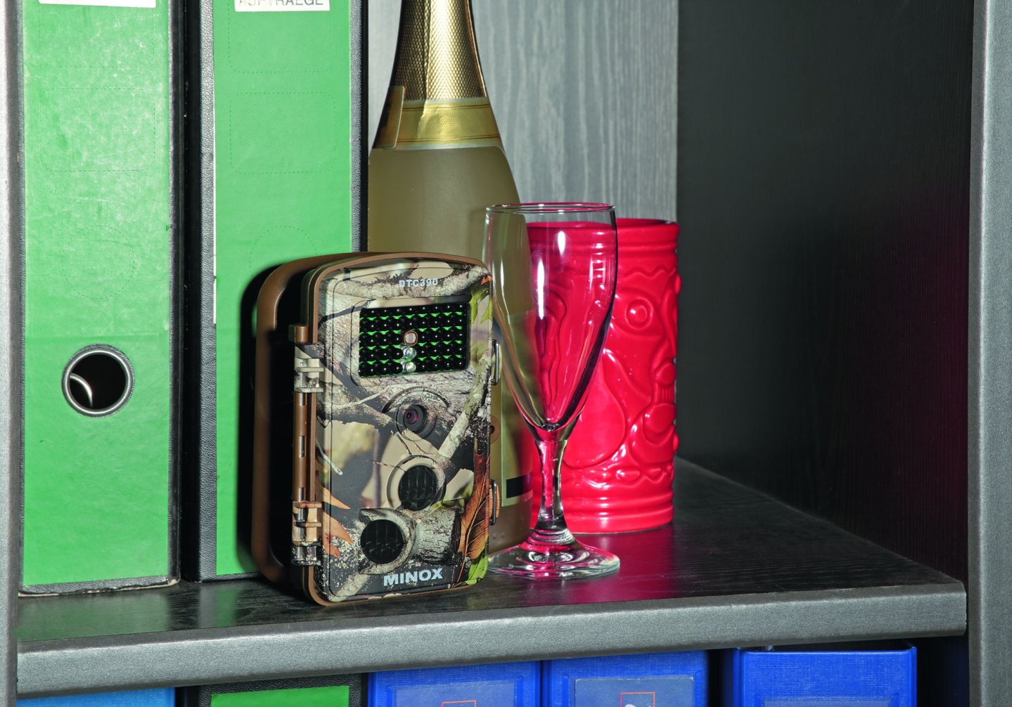 Wildkamera in einem Regal, neben Sekt und Sektglas.