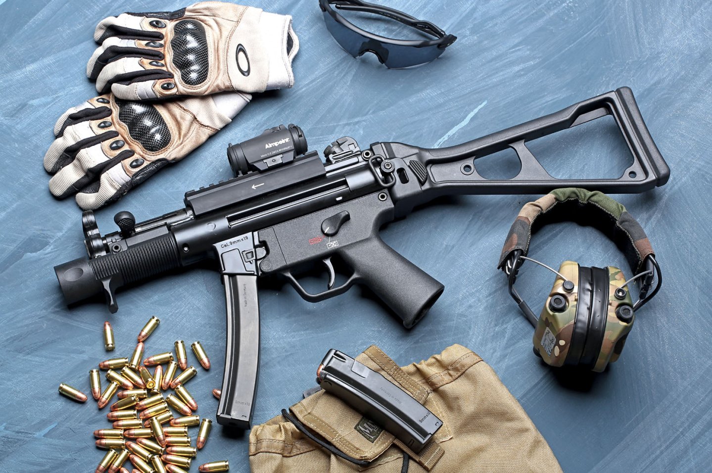caliber 7+8/2016 Heckler & Koch SP 5 K auf blau gemasertem Untergrund mit Handschuhen, Schießbrille, Gehörschutz, Munition und Ersatzmagazin.