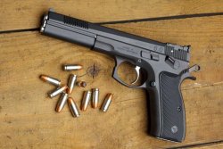 caliber 10/2017: Die brandneue CZ 75B 6.0 in 9x19 aus dem Hause AKAH ist eine grundsolide Ganzstahlwaffe mit sportlicher Ausstattung, die viel Leistung für kleines Geld bietet. CZ 75B in linker Seitenansicht mit Munition auf Holzbrett.