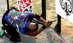 caliber 11+12/2017 Pistolenschütze in buntem T-Shirt auf den Knien mit um die Ecke gebeugtem Oberkörper.