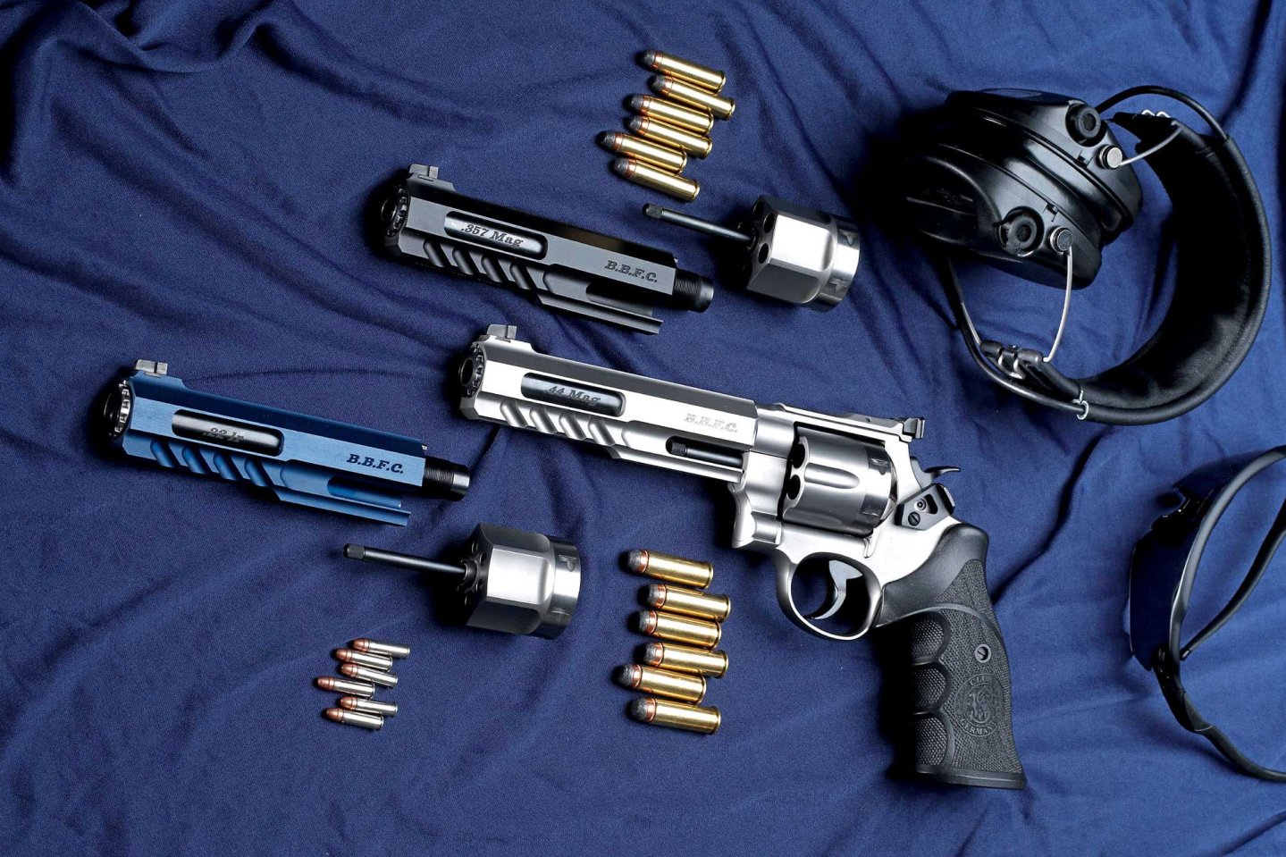 Der BBFC-Multikaliber-Matchrevolver vom S&W Club 30-Mitglied Thomas Spohr auf Basis des Smith & Wesson N-Rahmen-Modells 629 mit eingebautem .44 Magnum-System und danebenliegenden, einbaufertigen Wechselsystemen in .357 Magnum (links) und .22 Long Rifle (rechts) auf blauem Grund.