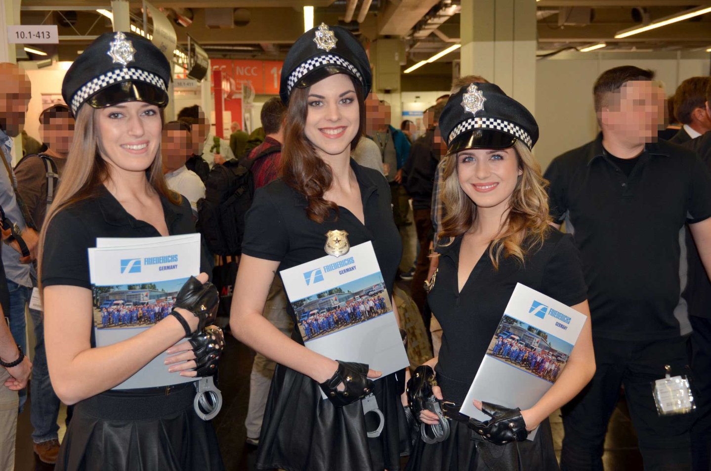 caliber 4/2017 Drei Messehostessen in Polizeiähnlichen Kostümen mit Handschellen begrüßen die Messegäste.