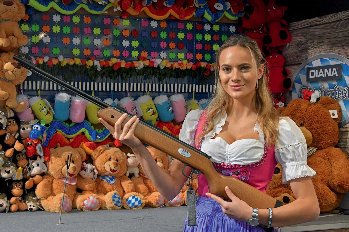 caliber 5/2018 Junge Frau im Dirndl präsentiert ein Diana Oktoberfest-Luftgewehr vor einer Schießbude.