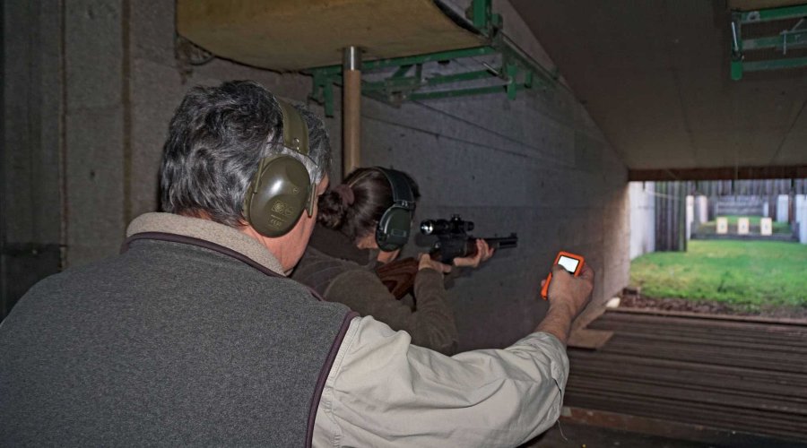 VISIER 5/2017 Eine Frau schießt einen Unterhebelrepetierer auf dem Schießstand, ein Mann hinter ihr stoppt mit einem Messgerät in der Hand die Zeit.