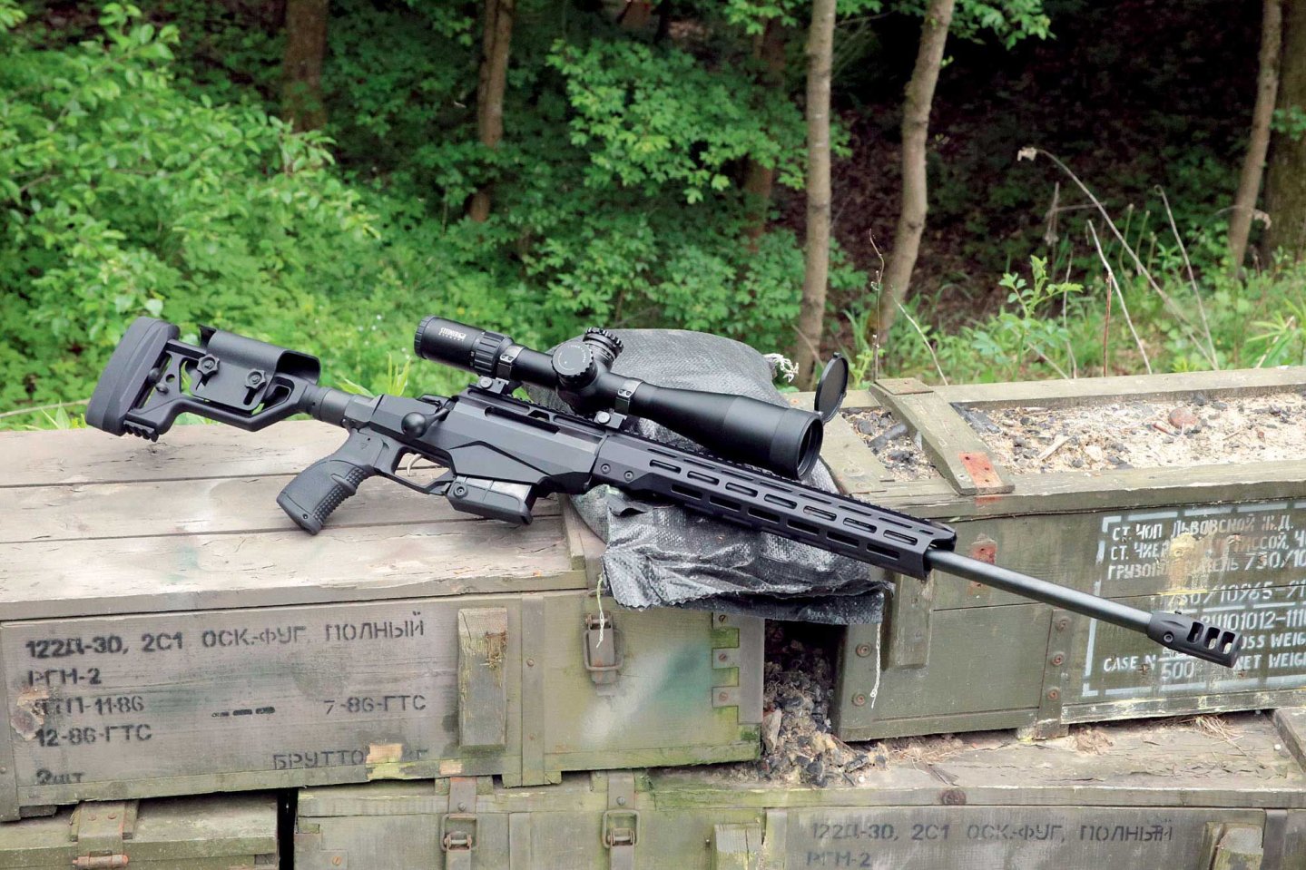 VISIER 7/2017 Tikka T3x TAC A1 in rechter Seitenansicht liegt auf alten Munitionskisten im Hintergrund ist Wald.