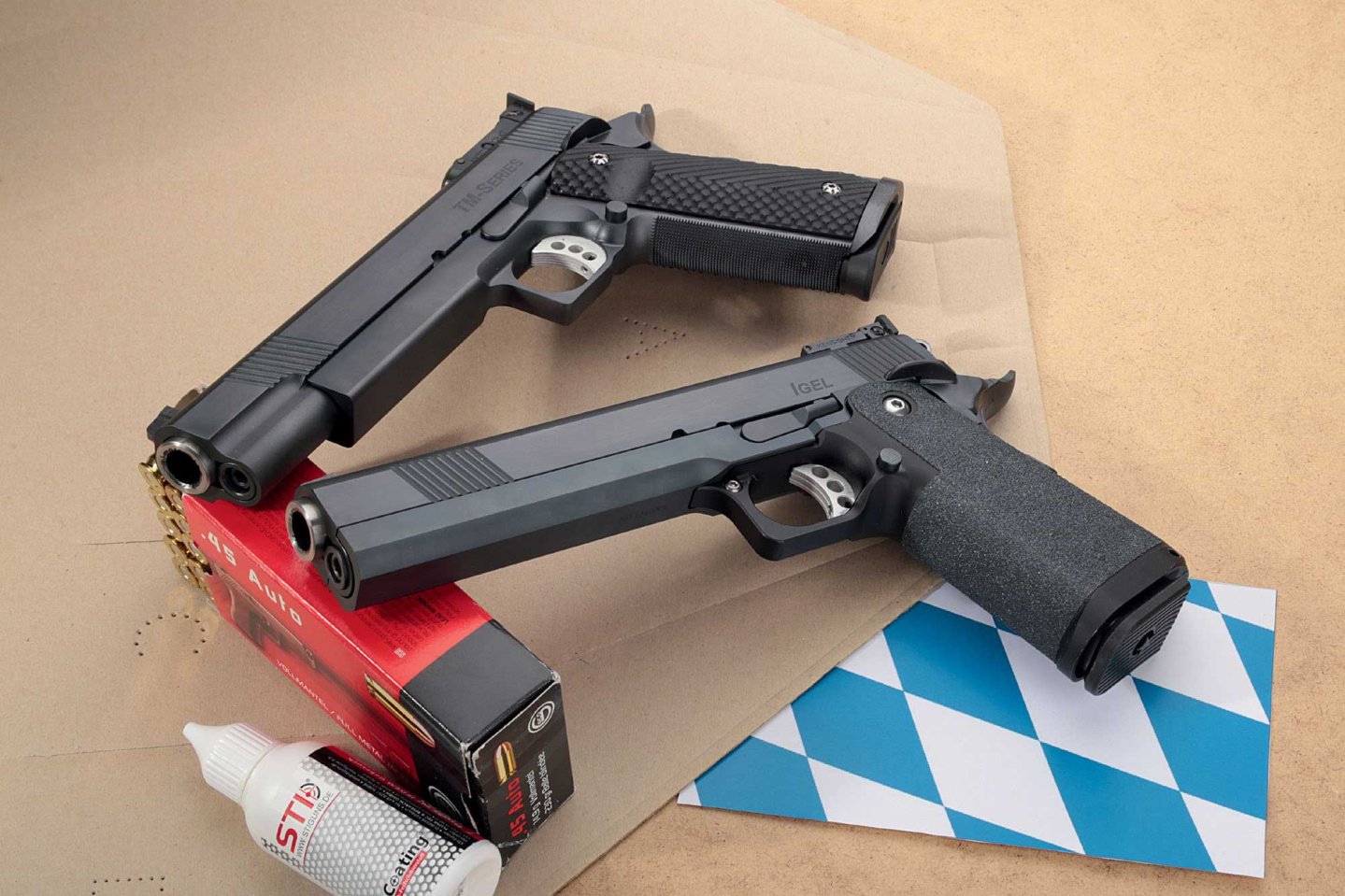 VISIER 4/2017 STI Europe TM-Series (oben) und STI Europe Igel (unten) in linker Seitenansicht angelehnt an eine Munitionspackung auf einer Zielscheibe und einer Serviette in bayerischen Farben.