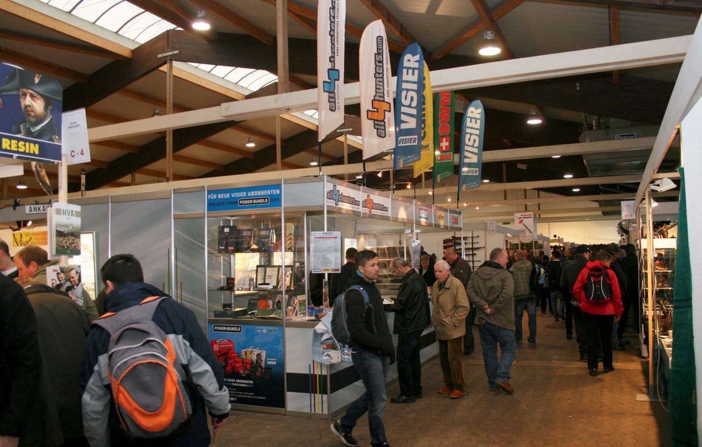 Besuchen Sie uns auf der Waffenbörse Kassel 2016 (WBK) Messestand mit bunten Fahnen und einige Messebesucher.