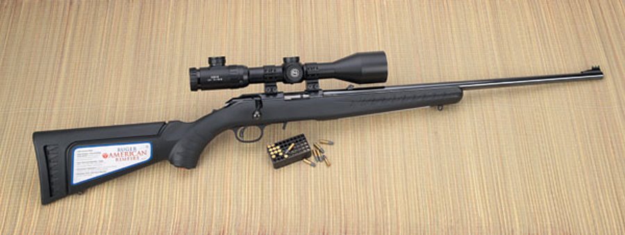 VISIER 6/2016 Ruger American Rimfire in rechter Seitenansicht auf Bastmatte mit Munition und aufgesetztem Zielfernrohr GECO 2,5-15x50 IR und großem Aufkleber auf dem Schaft.
