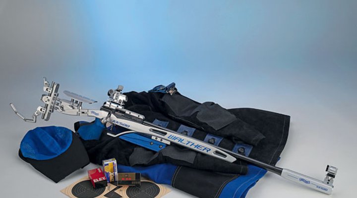 Das Walther KK 500 Expert in rechter Seitenansicht auf einer schwarz-blauen Schießjacke liegend, neben Mütze, Zielscheiben und drei verschiedenen Munitionspäckchen.