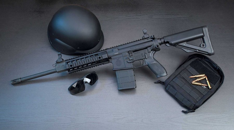 SIG Sauer 716 Patrol auf dunkelgrauem/schwarzen Hintergrund mit schwarzem Helm, Schießbrille und schwarzer Tasche.