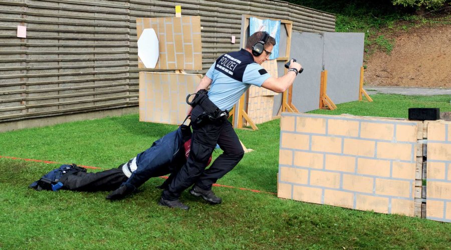 Polizist mit Pistole in der Hand schleift einen Dummy auf einem Pistolenparcours hinter sich her.