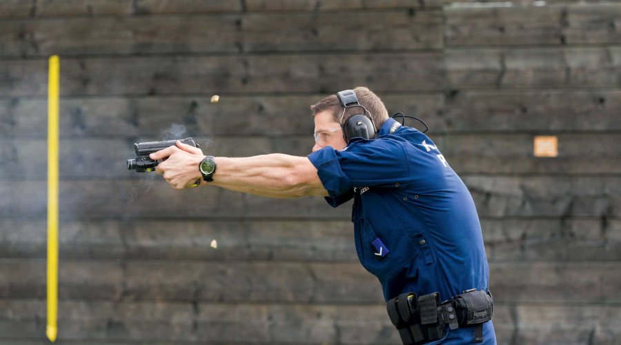 Polizist im Profil auf dem Schießstand, schießt mit der Pistole so schnell, dass sich zwei Hülsen in der Luft befinden.