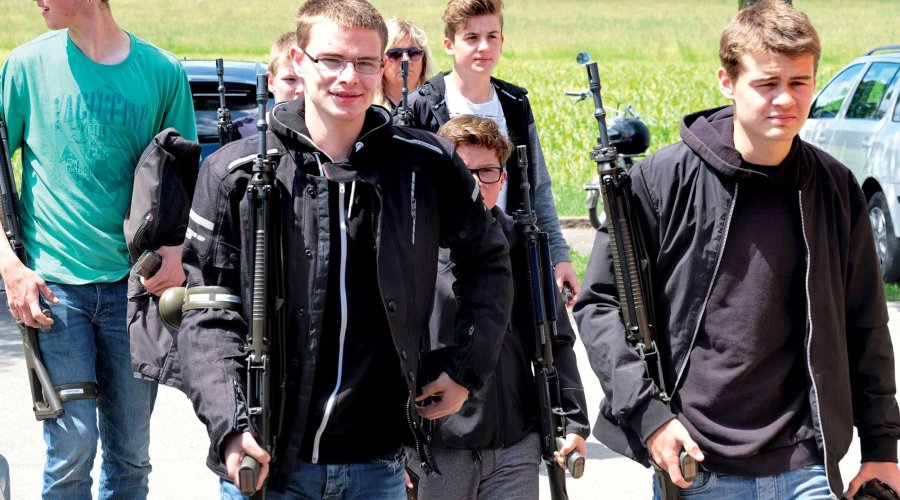 Mehrere junge Männer kommen mit ihrem Gewehr auf der Schulter zum Feldschiessen.