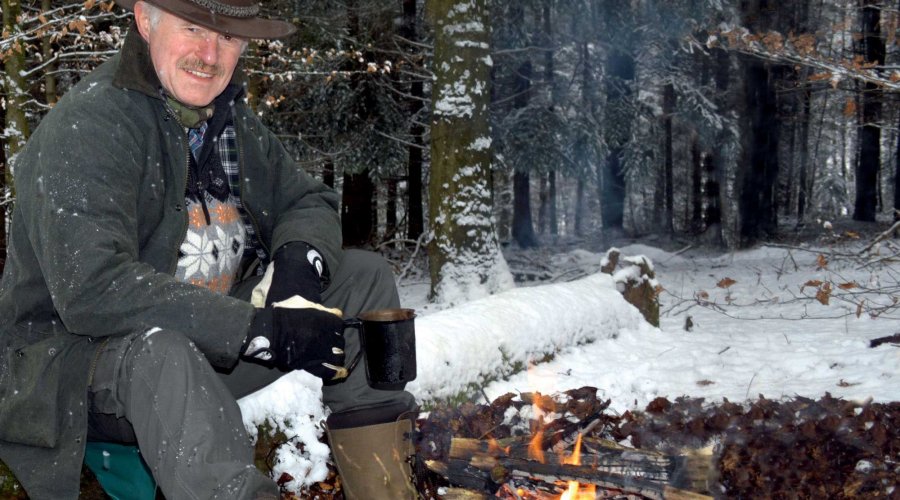 Walter Dold sitzt am Lagerfeuer im verschneiten Wald.