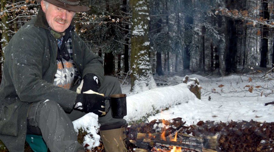 Walter Dold sitzt am Lagerfeuer im verschneiten Wald.