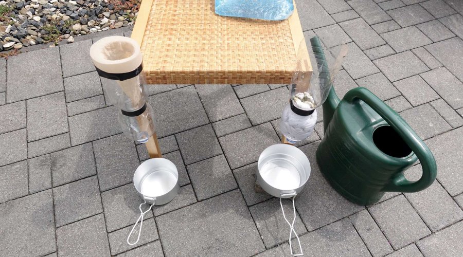 Filterstation bestehend aus Tisch, Gieskanne und abgeschnittenen Flaschen in einem Garten.