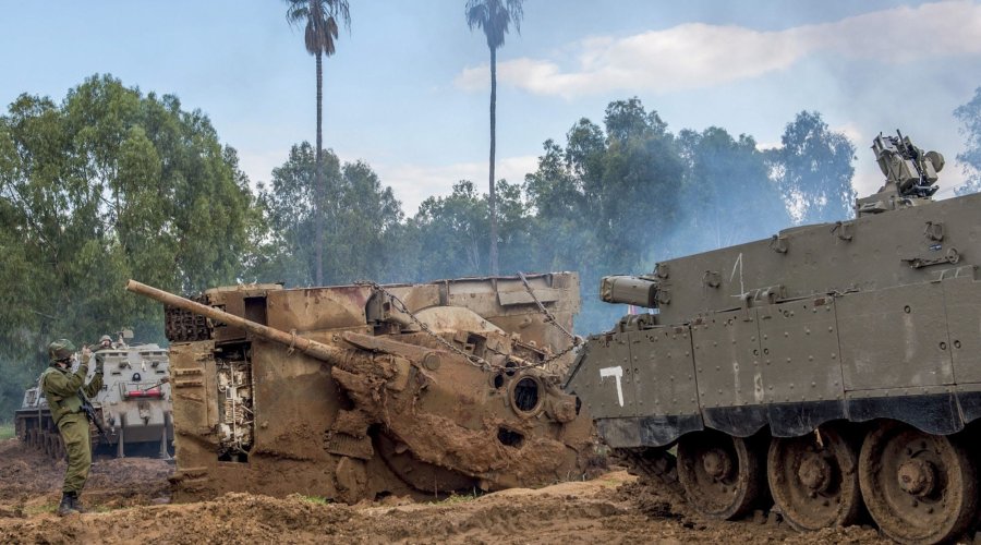 Ein Panzerwrack liegt auf seiner linken Seite im Matsch, ein Soldat steht davor und weist 2 Bergepanzer an.