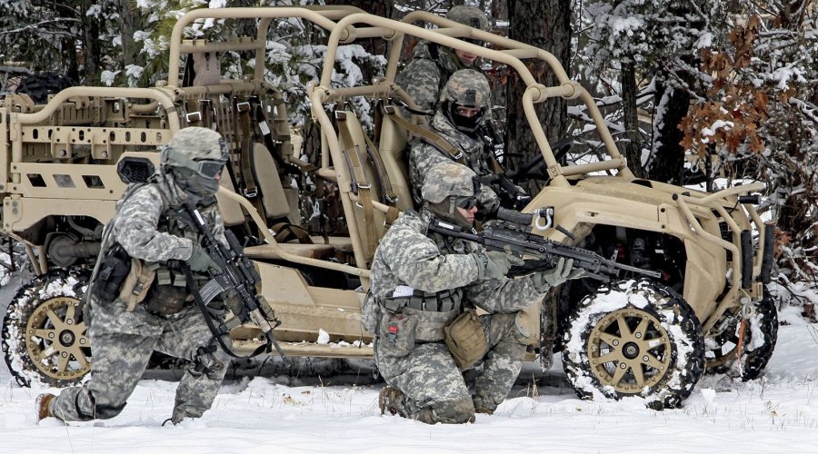 Ein Polaris MRZR steht vor einem Wald im Schnee. Ein Soldat sitzt darin, 3 sind abgestiegen, 2 davon knien mit ihren Sturmgewehren daneben im Schnee.