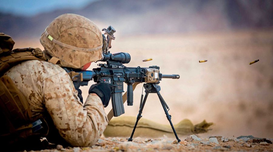 Soldat schießt HK416 auf Zweibein in der Wüste. Hülsen fliegen durch die Luft.
