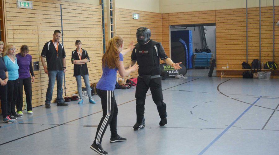 Eine Frau übt bei einem Selbstverteidigungskurs einen Angreifer abzuwehren.