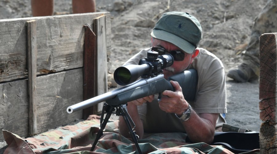 Schütze von schräg vorne gezeigt, hat ein Long-Range-Gewehr im Anschlag und blickt durch ein Kahles K1050.