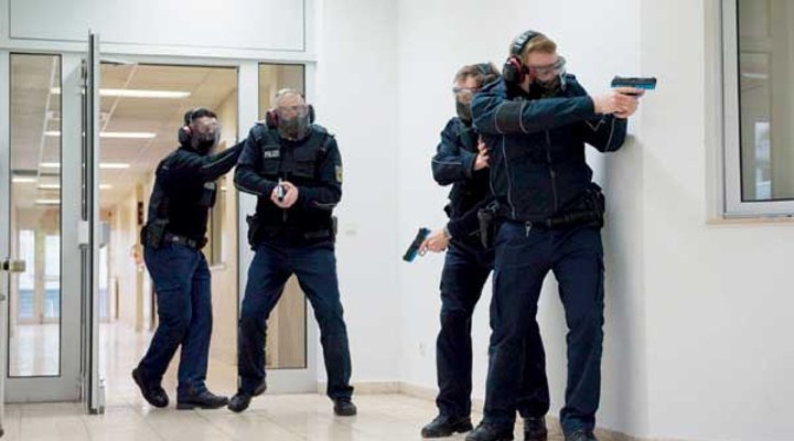 Vier Polizisten trainieren mit Übungswaffen auf einem Büroflur.