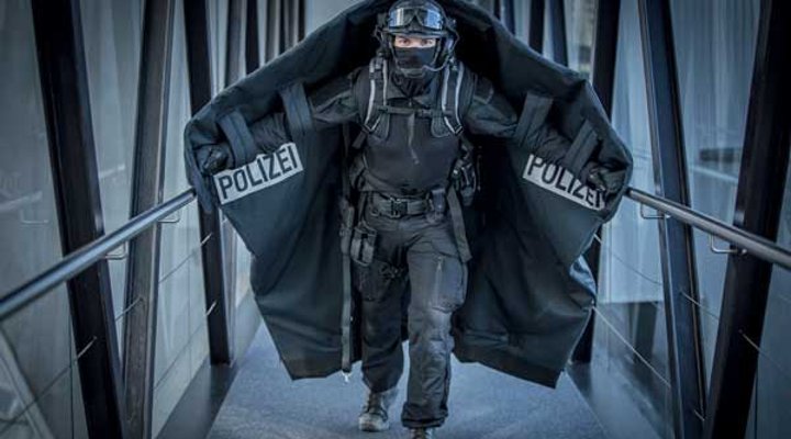 Polizist mit ausgebreiteter Geiselschutzdecke läuft einen Gang hinunter.