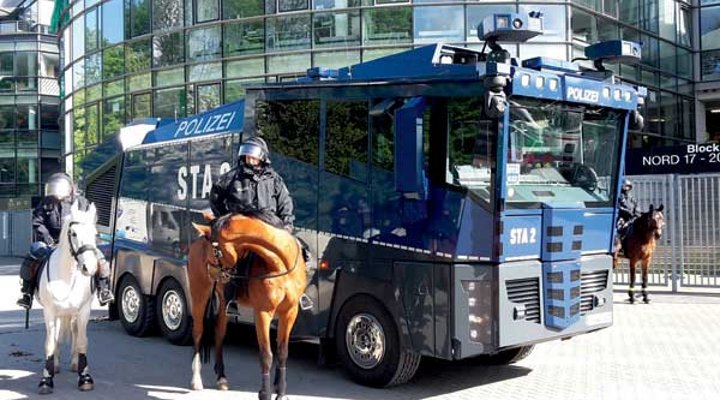 Wasserwerfer und Polizisten zu Pferde stehen vor einem Fußballstadion.